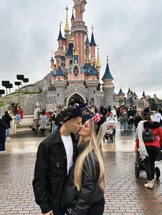 a man and woman kissing in front of a castle with lots of people around it