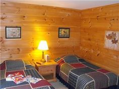 two beds in a room with wood paneling on the walls and lamps on either side