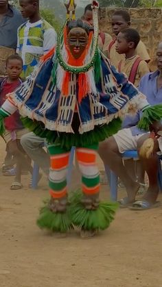 a group of people sitting and standing around a man in a colorful costume with feathers on his head