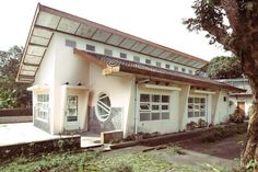 a small white building with lots of windows next to a tree and grass covered ground