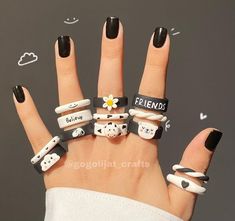 a woman's hand with black and white nail polish holding five rings that say friends