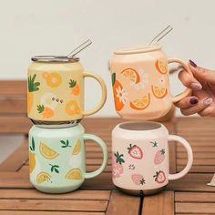 three mugs with strawberries, oranges and lemons on them sitting on a wooden table