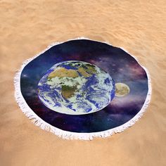 a round beach towel with the earth on it in the middle of sand and water