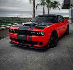 a red and black dodge car parked in front of a tall building with palm trees