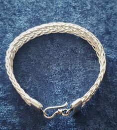 a braided bracelet is shown on a blue cloth with a metal hook in the middle