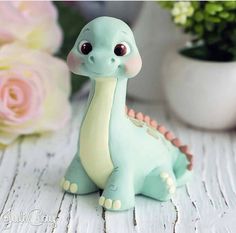 a small toy dinosaur sitting on top of a white wooden table next to flowers and a potted plant