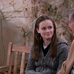 an older man sitting next to a young woman on a wooden bench in front of a tree