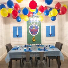 a party room with balloons and decorations on the ceiling, including blue table cloths