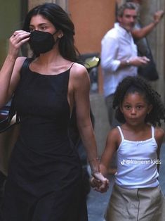 a woman and child walking down the street with masks on their faces as people walk by