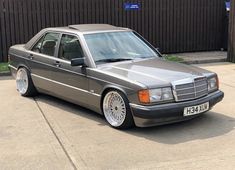 a silver car parked in front of a black fence and brown brick wall behind it