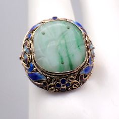 Vintage Chinese silver ring in floral filigree designs with vermeil finish and colorful enamel decorations, featuring carved oval green Jade centerpiece. The size is adjustable. This gorgeous ring is a size 7 1/4 (adjustable), 24 mm at the widest and weighs 6.5 grams. It features some enamel loss. EA2362 Oval Green Enamel Ring Gift, Green Oval Enamel Ring For Formal Occasions, Formal Green Oval Enamel Ring, Formal Oval Green Enamel Ring, Green Enamel Ring For Wedding, Green Enamel Jewelry For Wedding, Green Enamel Jewelry With Gemstones, Green Enamel Wedding Jewelry, Oval Cabochon Enamel Ring Collectible