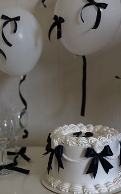 a white cake sitting on top of a table next to balloons