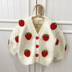 a white sweater with red strawberries on it hanging from a hook in front of a door