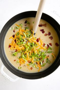 a bowl filled with soup and cheese on top of a white countertop next to a wooden spoon