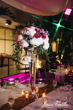 a tall vase filled with white and red flowers on top of a dining room table