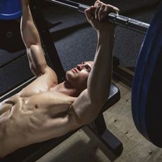 a shirtless man lifting a barbell in a gym with his hands behind his head