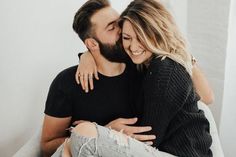 a man and woman cuddle together on a bed in front of a white wall