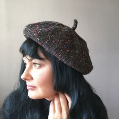 a woman with black hair wearing a knitted hat and holding her hand to her ear