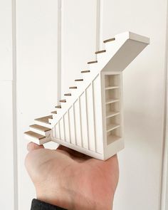 a hand holding a model of a house with stairs going up it's side