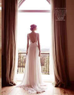 a woman standing in front of a window wearing a white dress and looking out the window