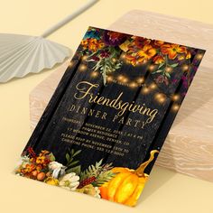 a thanksgiving dinner party card with pumpkins and flowers on it next to a fan