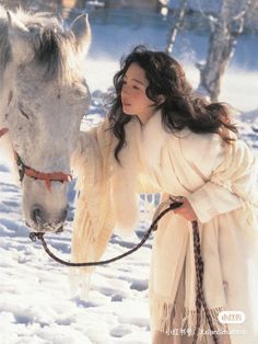 a woman standing next to a white horse in the snow