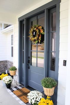 the front door is decorated with yellow and white flowers, wreaths and potted plants