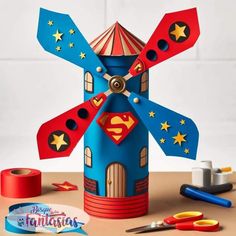 a paper windmill with some scissors and tape on the table next to it is an image of superman's house