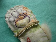 an old hand made mitt is on a green cloth covered with white fabric and has been stitched to the side