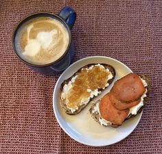 a white plate topped with two pieces of bread next to a cup of cappuccino