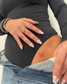 a pregnant woman's belly with a butterfly tattoo on her left side, in jeans