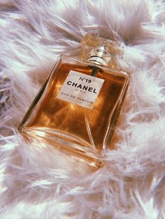 a bottle of chanel perfume sitting on top of a white fur covered bed sheet