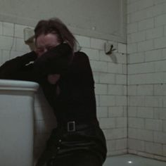 a woman sitting on the edge of a toilet in a bathroom next to a white tiled wall