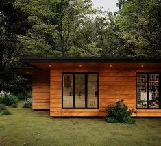 a small wooden cabin in the middle of some grass and trees with open windows on each side