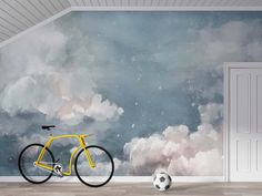 a yellow bicycle parked next to a soccer ball in front of a wall with clouds painted on it