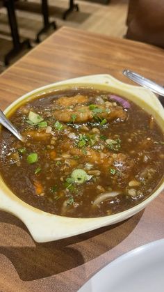 a white bowl filled with soup on top of a wooden table next to two spoons