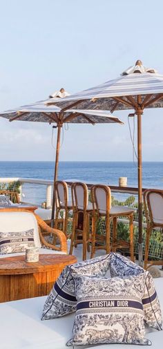 an outdoor seating area with chairs and umbrellas overlooking the ocean on a sunny day