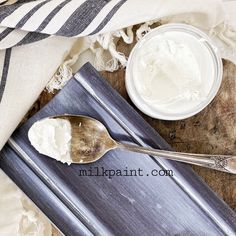 two spoons with white cream sitting on top of a wooden table next to a cloth