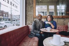 a man and woman sitting at a table in front of a window with coffee cups