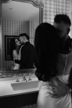 a man and woman kissing in front of a bathroom mirror while another person takes a photo