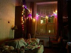 a living room filled with furniture covered in blankets and christmas lights on the windowsill