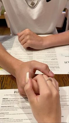 two people sitting at a table with papers and pens in front of them, one holding the other's hand