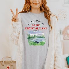 a woman wearing a welcome to camp crystal lake t - shirt while holding up her peace sign