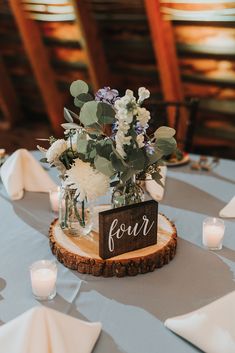 a centerpiece with flowers and greenery is displayed on a wooden slice at the head table