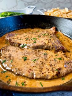 two steaks are in a skillet with gravy