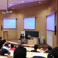 an auditorium with people sitting on the floor and one person standing up in front of them