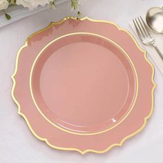 a pink plate with gold trim sits on a white tablecloth next to silverware