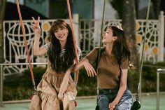 two young women sitting on swings and smiling at each other's eyes while one holds her hand up in the air