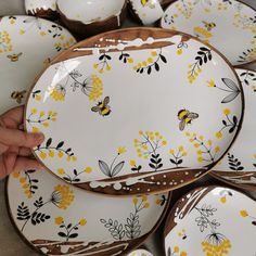 a bunch of plates with yellow flowers and bees on them are being held by someone's hand