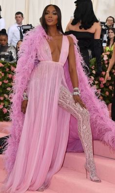 a woman in a pink gown and feathered coat sitting on steps at the mete